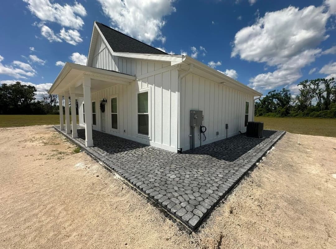 Modern white house with gray stone pathway under a blue sky and scattered clouds.