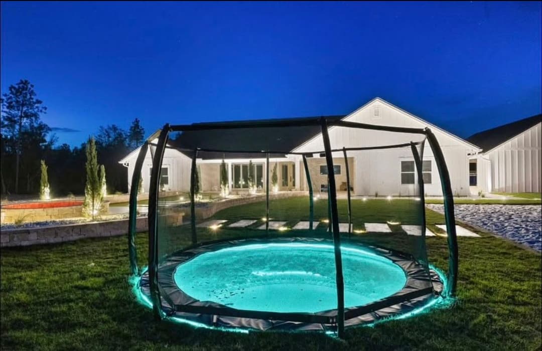 Modern home at night featuring a glowing trampoline in a landscaped yard.