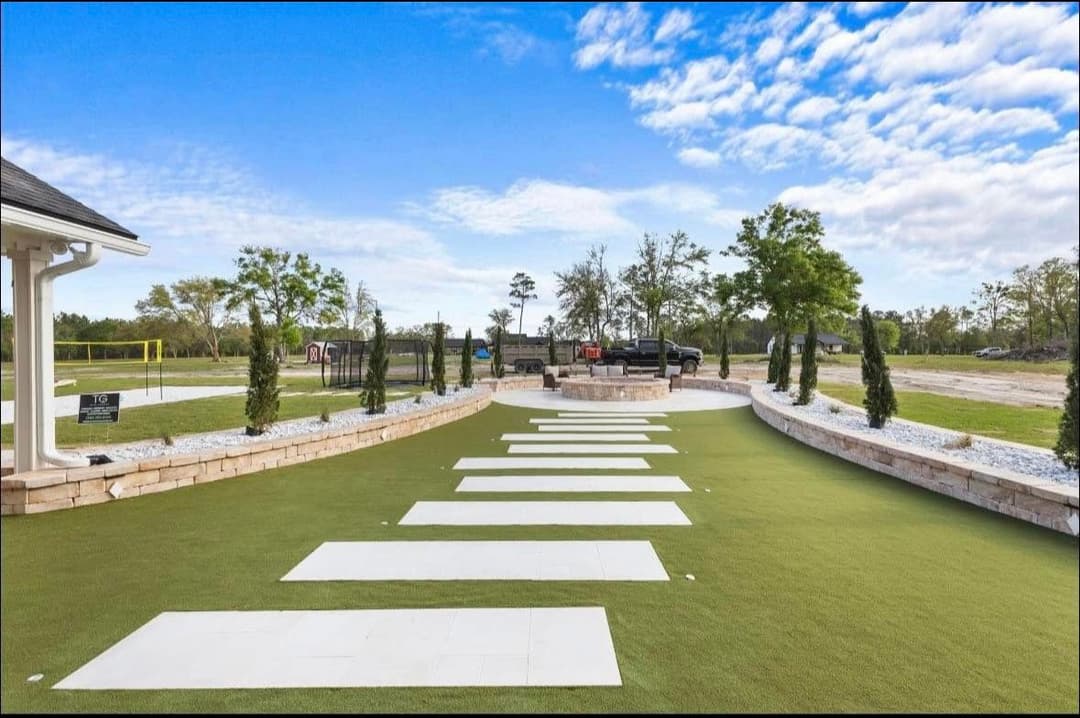 Modern outdoor event space with green lawn, stone pathways, and seating area under a blue sky.