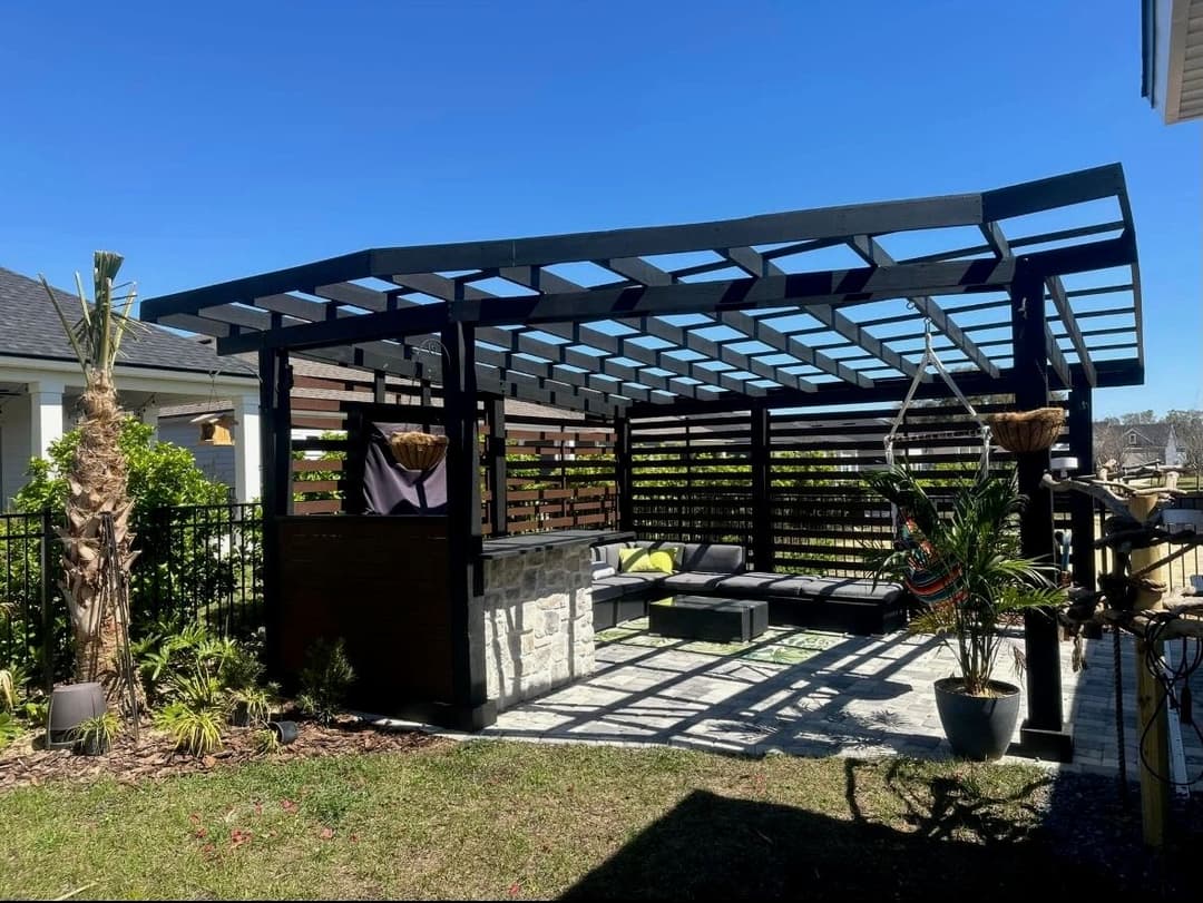 Modern outdoor pergola with seating area, greenery, and bright blue sky. Ideal for relaxation.