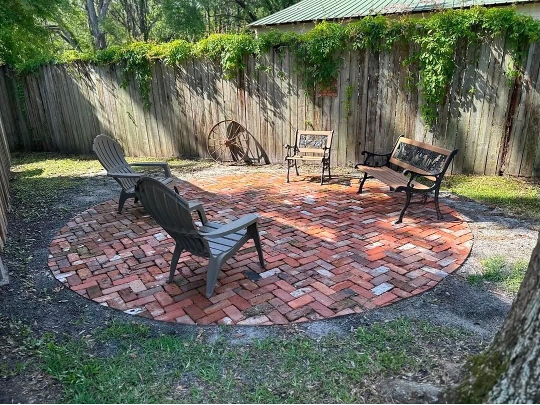 Patio seating area with brick circular pavers, surrounded by wooden fence and greenery.