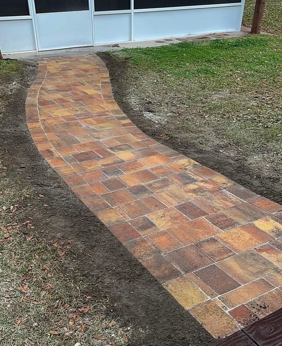Curved brick pathway lined with grass, leading to a glass door, enhancing outdoor aesthetics.
