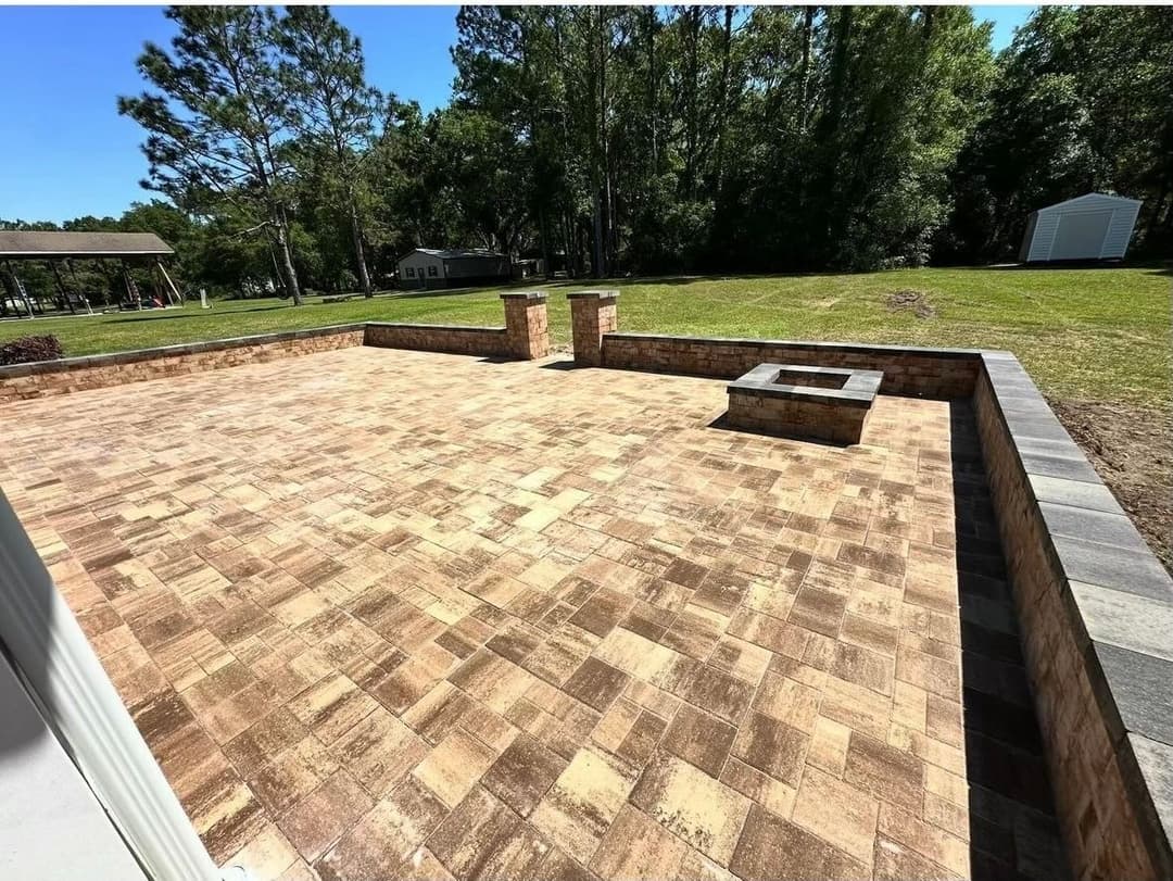 Patio area with paver stones, landscaped greenery, and fire pit in a residential backyard.