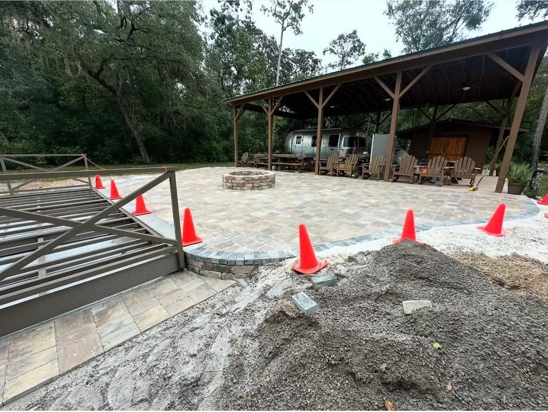 New outdoor patio area with stone pavers, seating, and safety cones in a wooded setting.