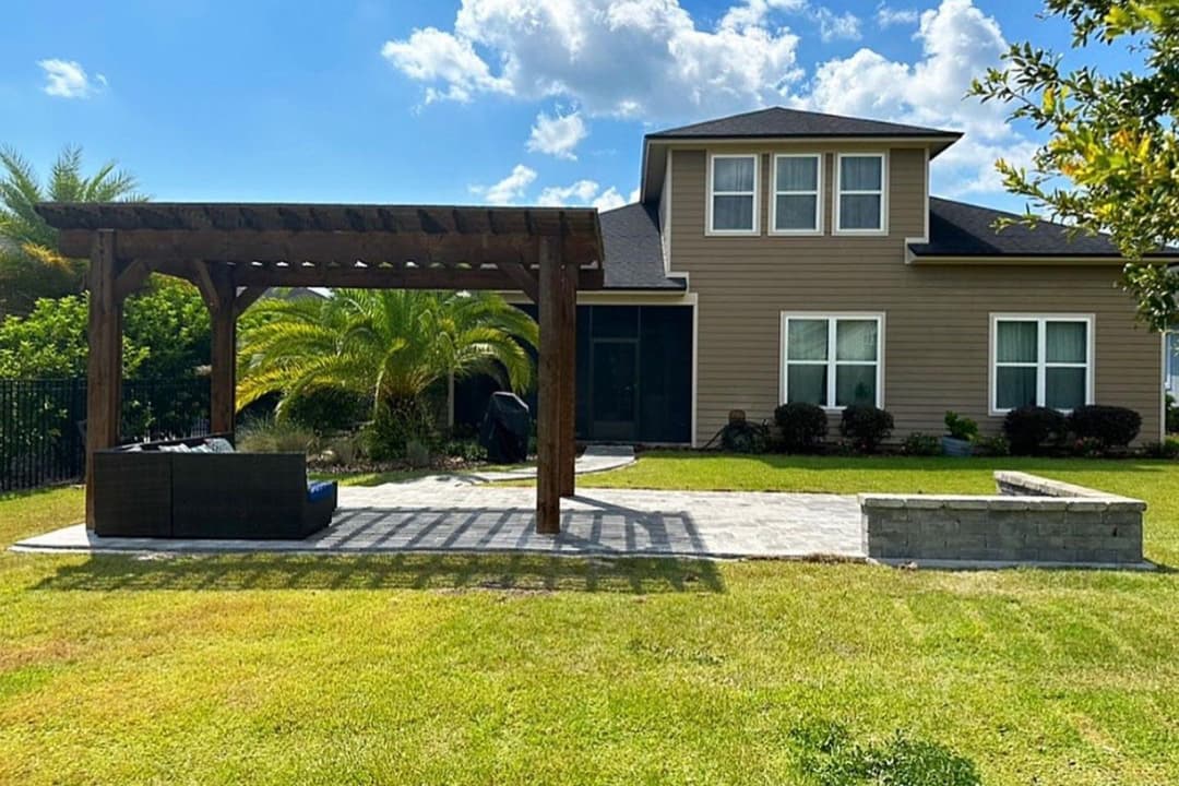 Modern home exterior with patio, pergola, and landscaped lawn under a blue sky.
