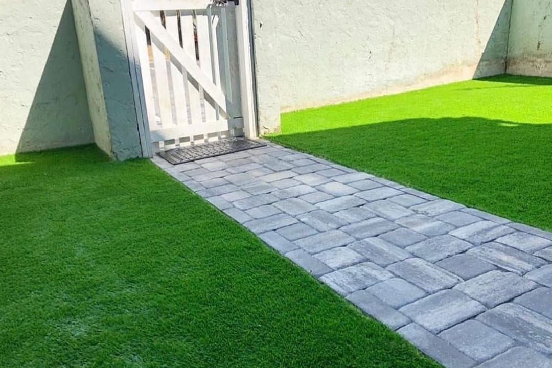 Lush green lawn with a stone pathway leading to a white gate.