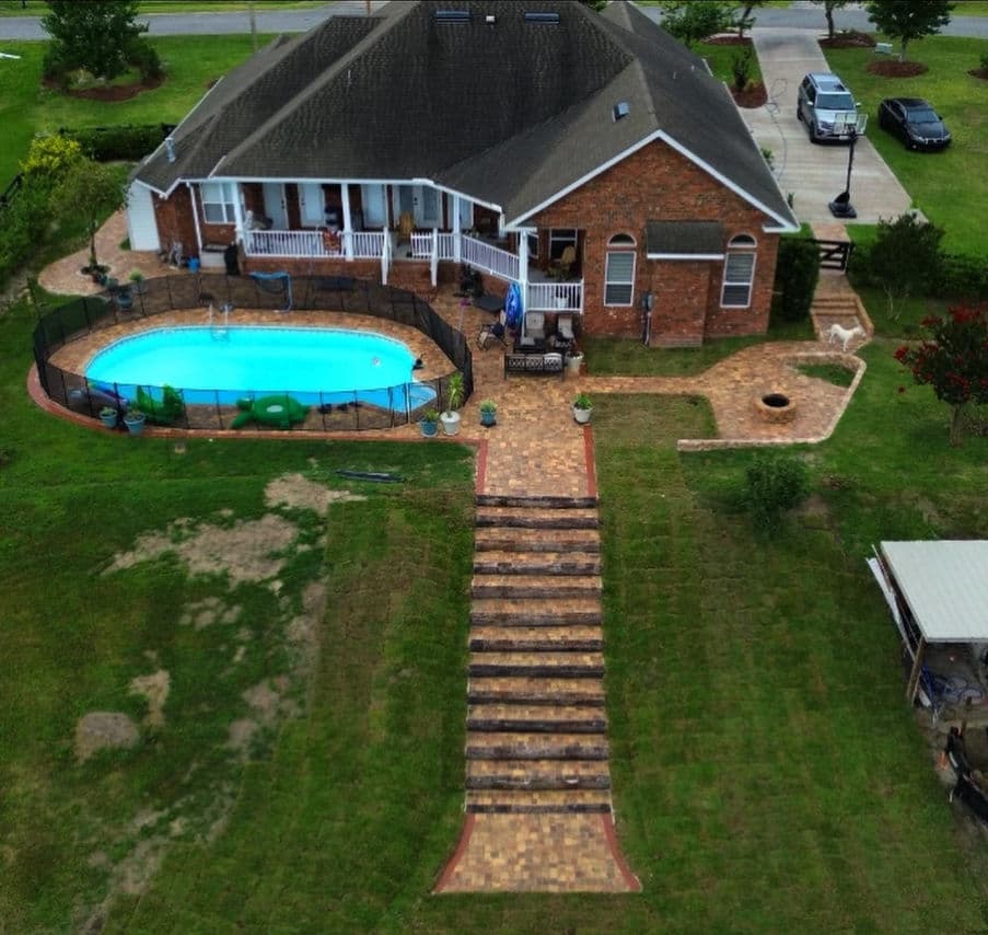 Aerial view of a home with a pool, lawn, and landscaped patio. Pathway leading to entrance.