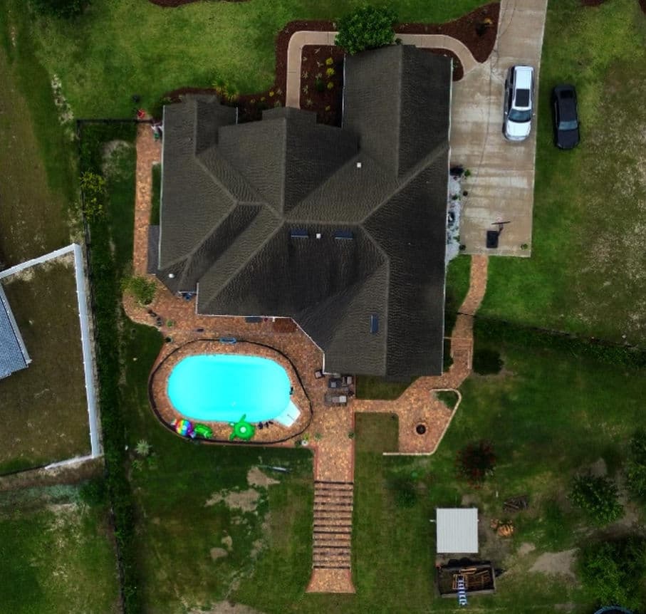 Aerial view of a house with a pool, surrounded by a landscaped yard and driveway.