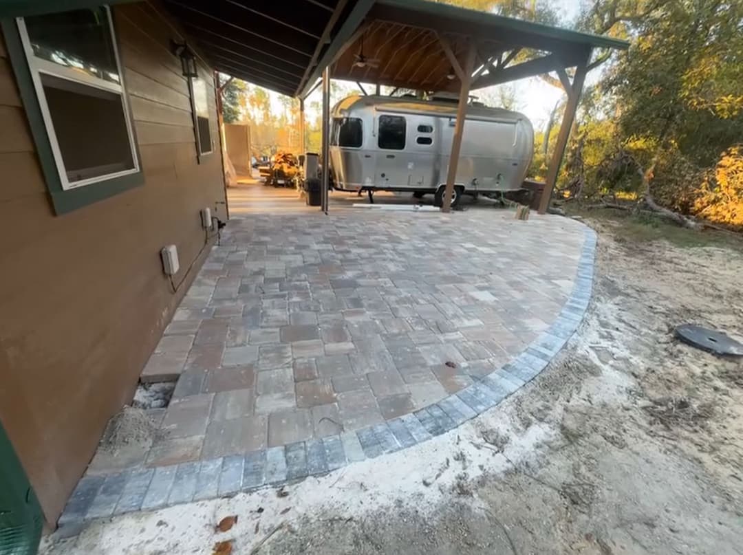 Paved outdoor patio with curved border next to Airstream and wooden structure.