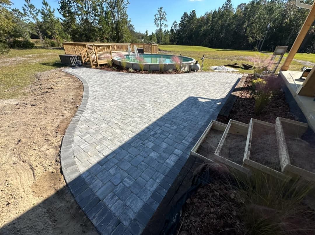 Curved stone patio with hot tub and wooden deck in a serene outdoor setting.