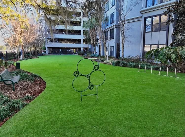Green lawn area with decorative circular sculpture and nearby benches in a modern building setting.