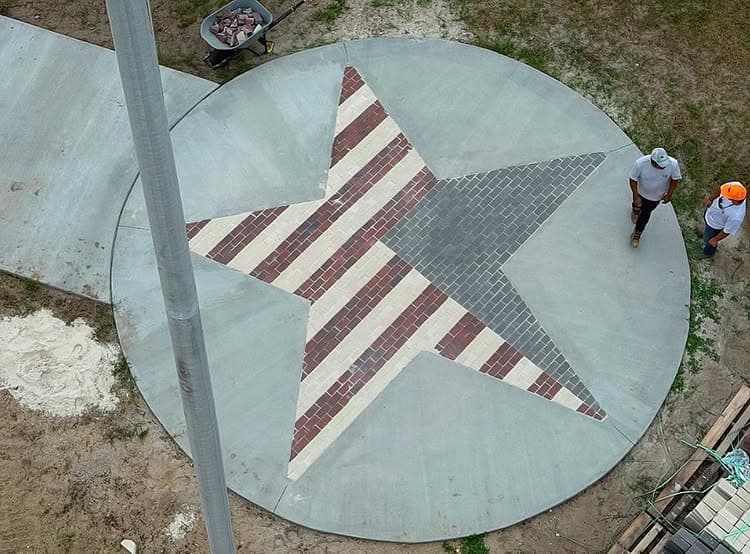 Circular concrete design featuring a star pattern in red, white, and gray bricks with workers nearby.