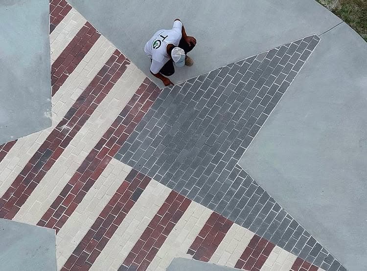 Worker installing decorative brick pattern in the shape of a star on pavement surface.