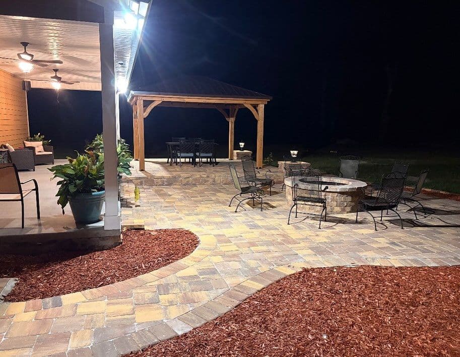 Cozy outdoor patio at night with fire pit, seating areas, and garden features.