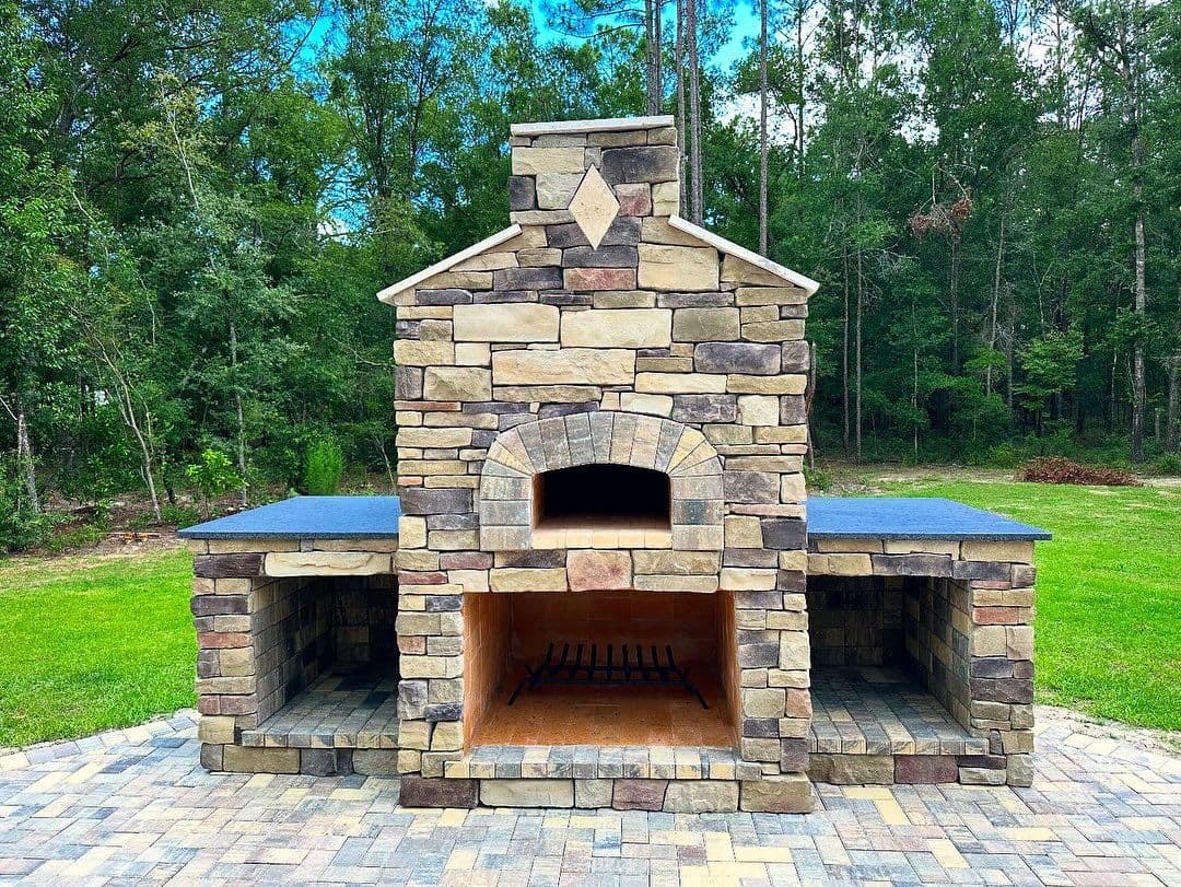 Stone outdoor pizza oven with grilling space, set in a lush green garden. Ideal for cooking.