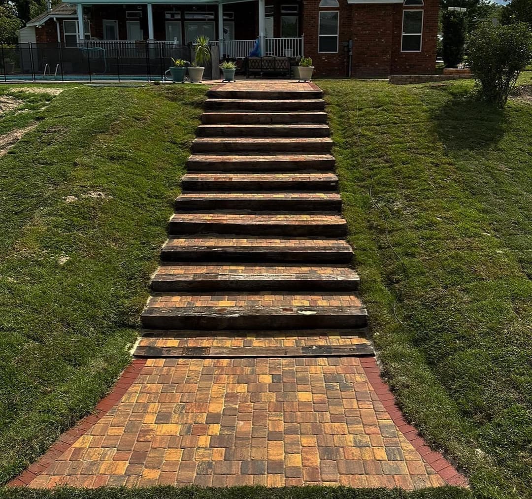 Stone pathway with steps leading up a grassy hill to a house, surrounded by landscaping.
